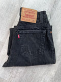 Vintage black Levi's 551 relaxed fit tapered leg jeans displayed on a wooden surface, showcasing the fabric and stitching details.