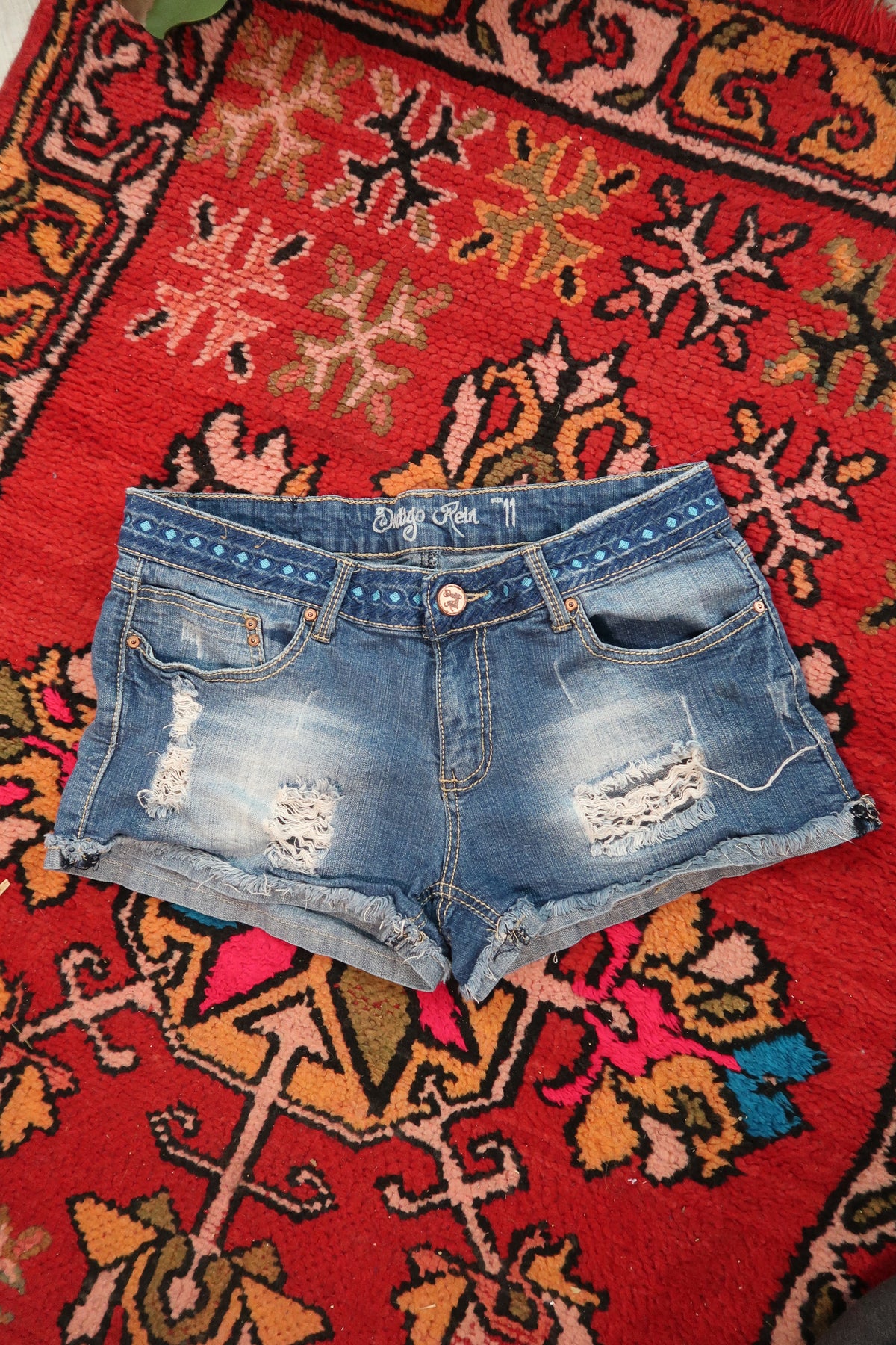 Distressed denim shorts for women with embroidered waistband by Elektra Vintage, showing frayed edges and colorful embroidery detail.