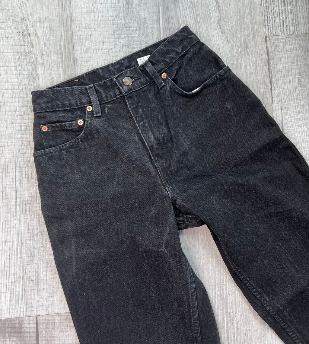 Vintage black Levi's 551 relaxed fit tapered leg jeans displayed on a wooden surface with a casual folded design.