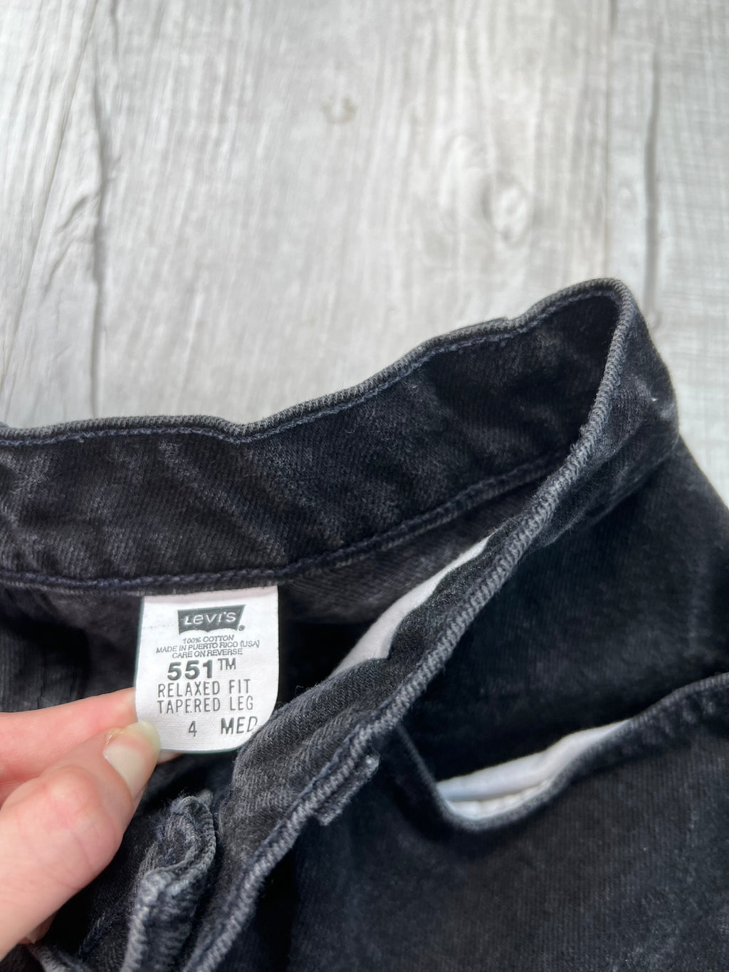 Vintage black Levi's 551 relaxed fit tapered leg jeans displayed on a wooden surface with a rustic background.