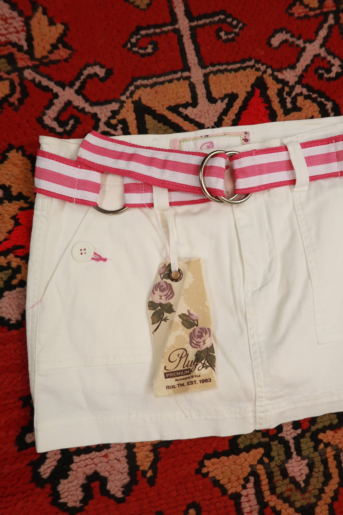 Vintage white denim mini skirt with pink stripe belt by Elektra Vintage, Y2K style, shown on a hanger.
