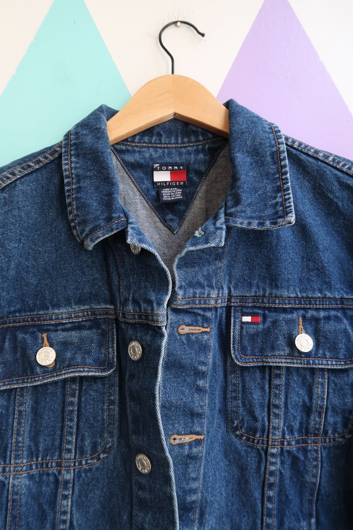 Vintage Tommy Hilfiger denim jacket from the 2000s, classic blue jean trucker style, displayed on a hanger.