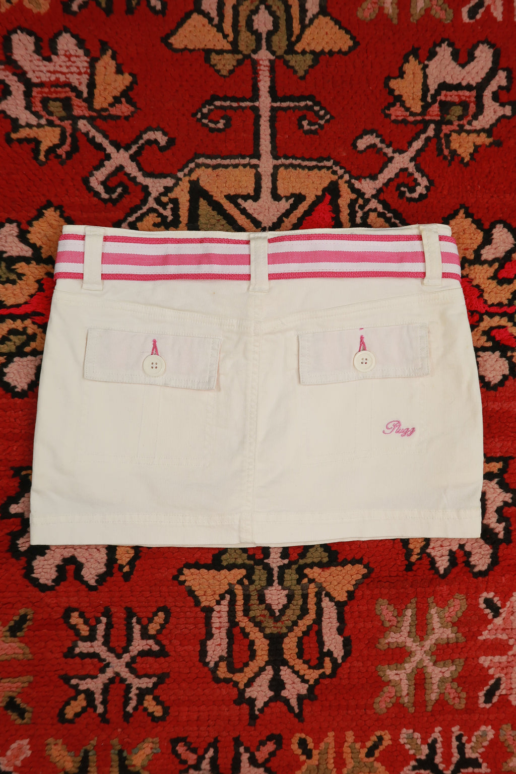 Vintage white denim mini skirt with pink stripe belt from Elektra Vintage, Y2K style, shown on a hanger.