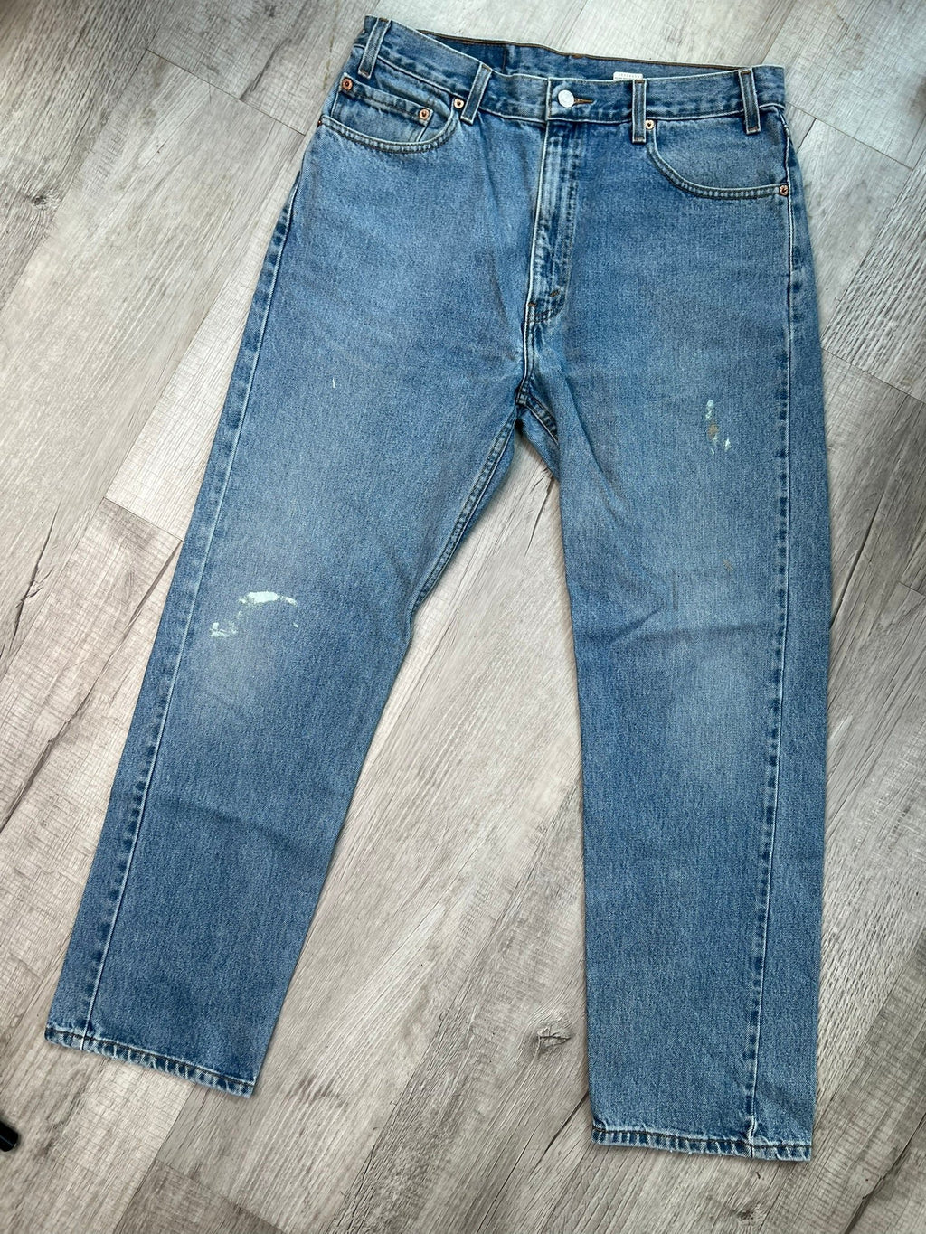 Men's Levi’s 505 regular fit straight leg jeans with medium wash and paint splatter detail, displayed on a hanger.