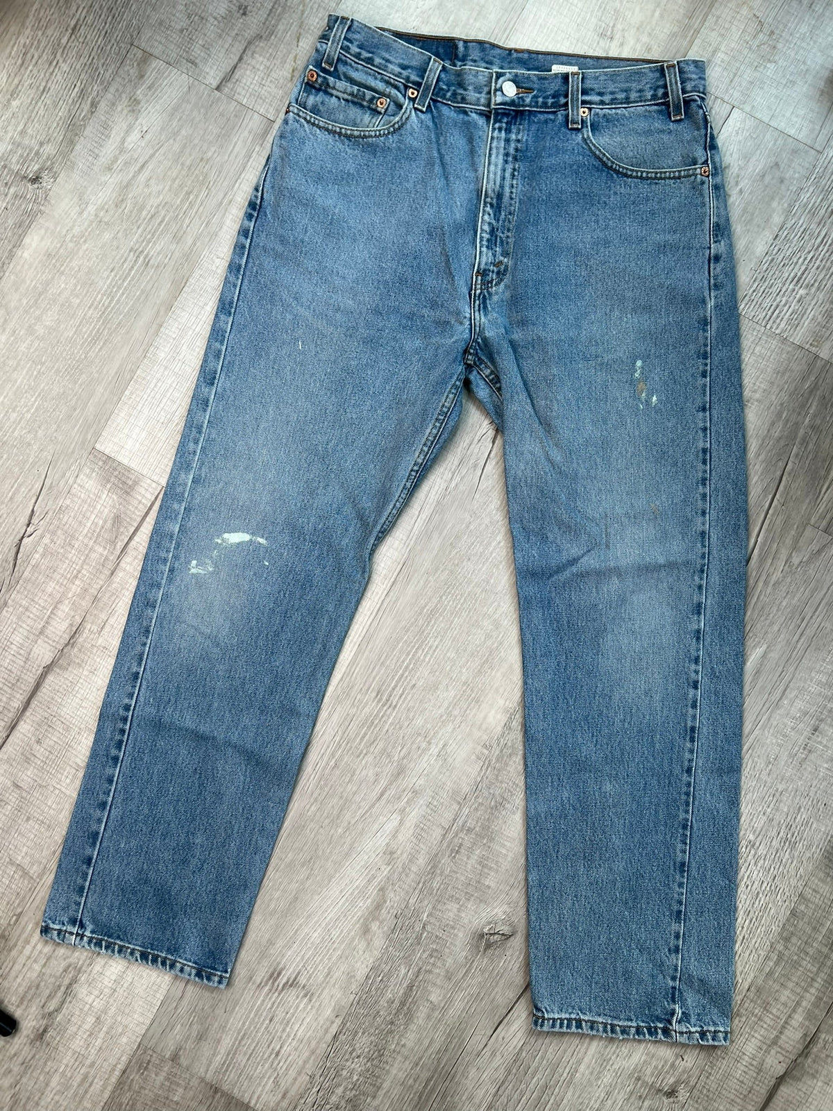 Men's Levi’s 505 regular fit straight leg jeans with medium wash and paint splatter detail, displayed on a hanger.