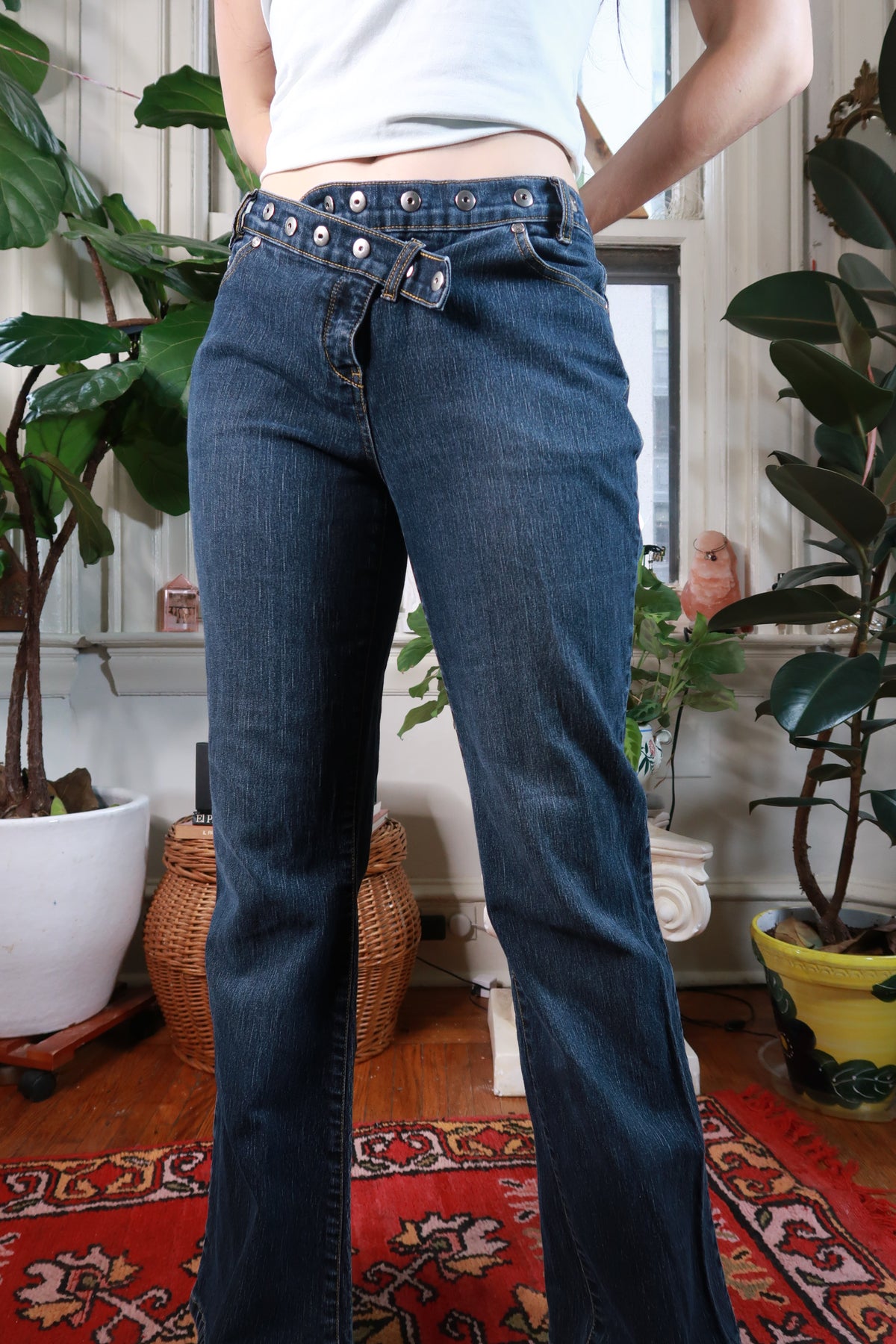 Dark wash low rise flare jeans with grommet belt detail from Elektra Vintage, vintage 2000s women's bottoms displayed on a hanger.