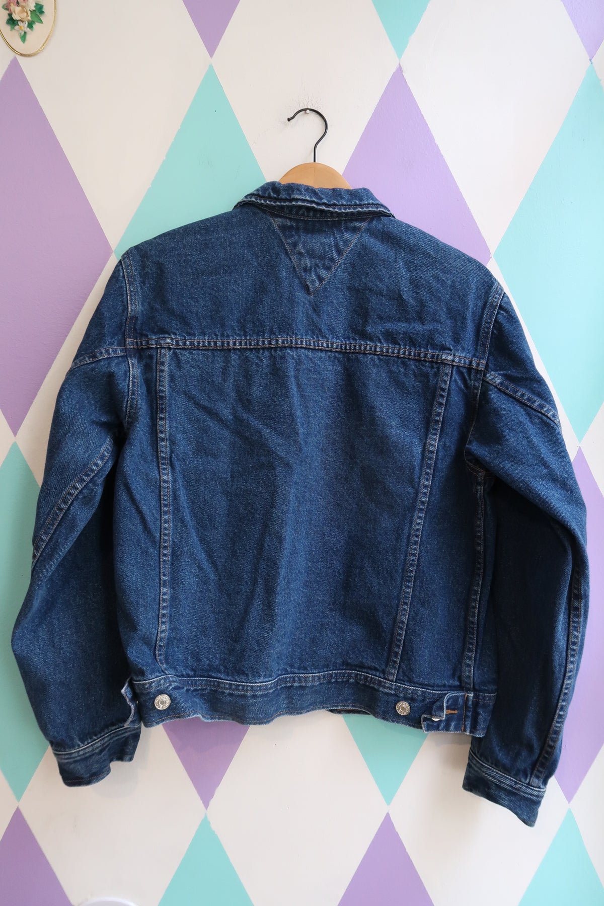 Vintage Tommy Hilfiger denim jacket from the 2000s featuring classic blue jean trucker style, shown on a hanger.
