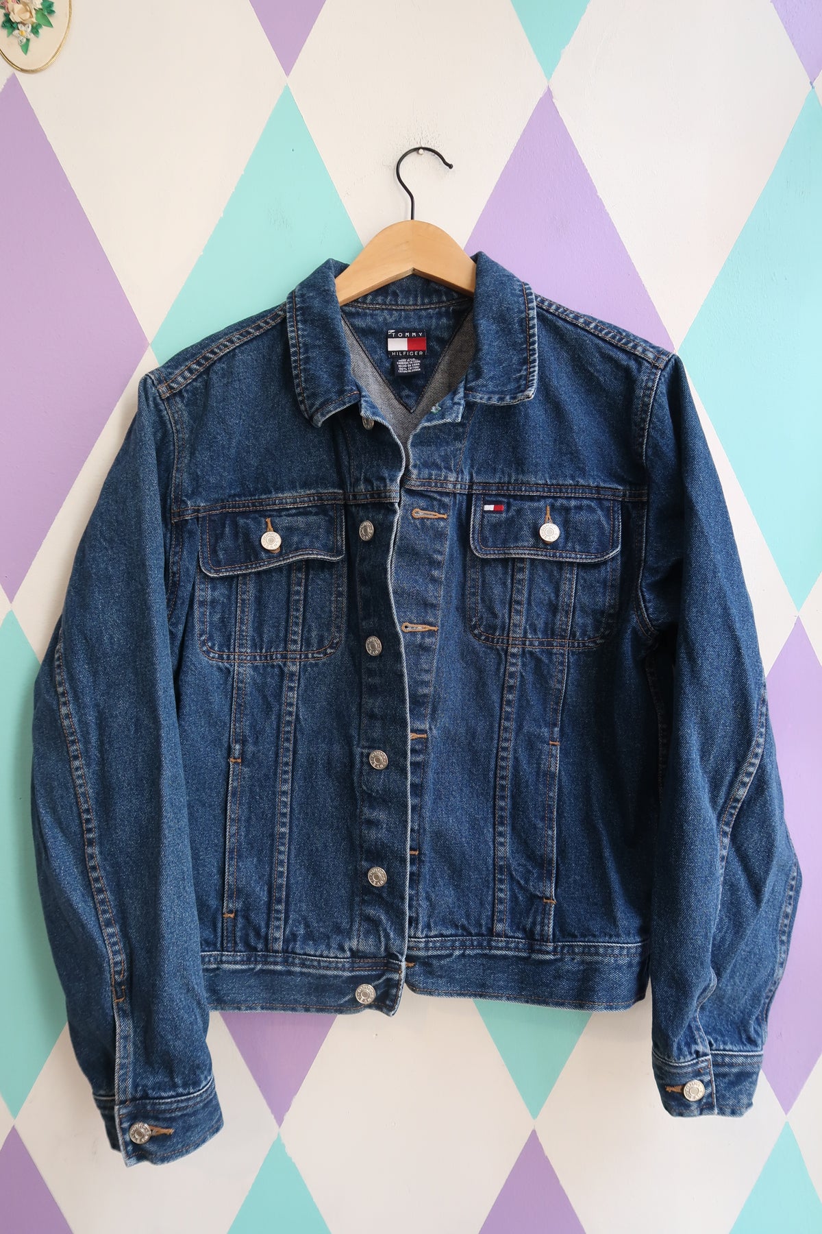 Vintage Tommy Hilfiger denim jacket, 2000s classic blue jean trucker style, with visible button closures and distressed details.