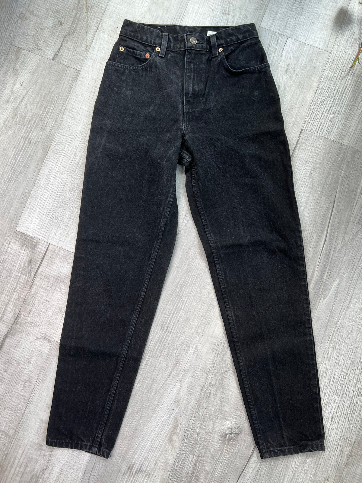 Vintage black Levi's 551 relaxed fit tapered leg jeans displayed on a wooden surface, showcasing the fabric and stitching details.