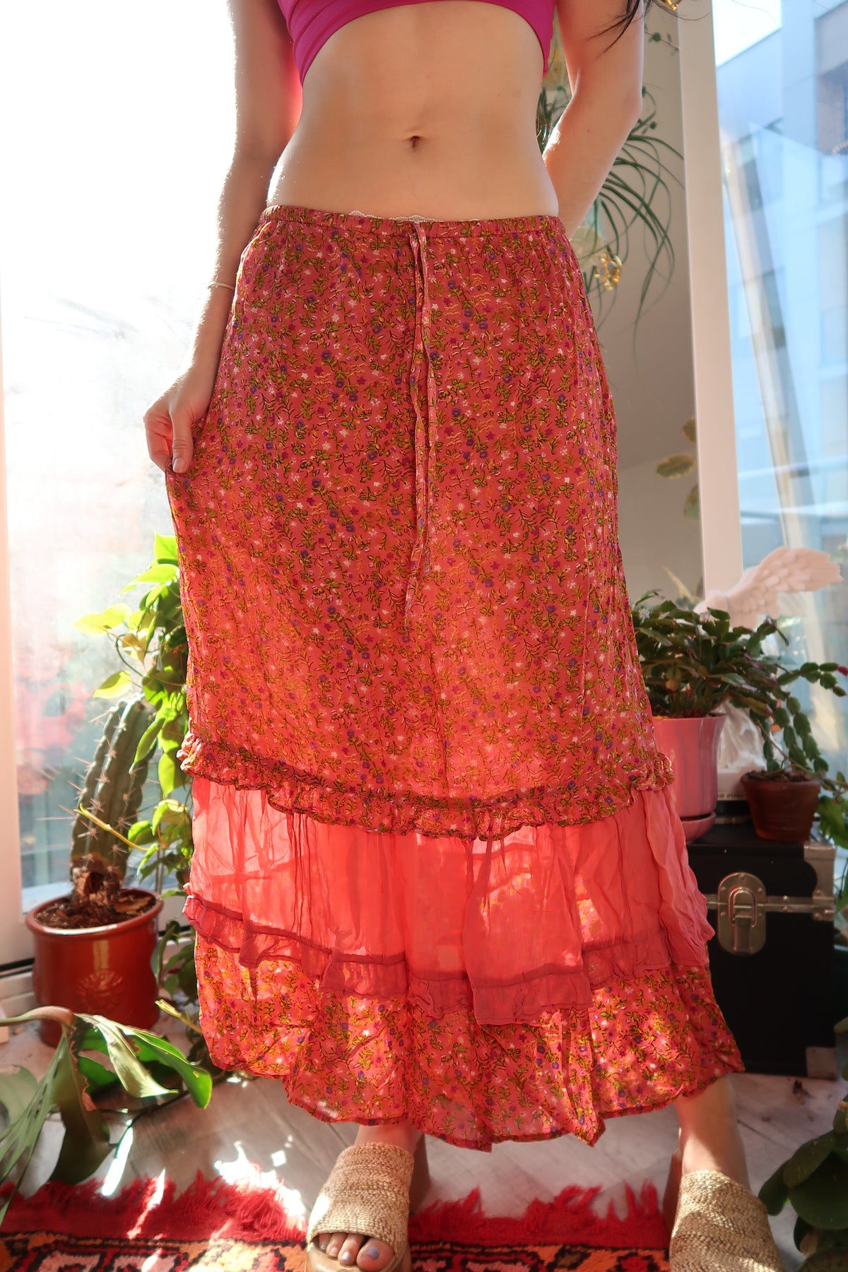 Vintage pink floral tiered midi skirt by Elektra Vintage displayed on a hanger with ruffled layers and a floral pattern.