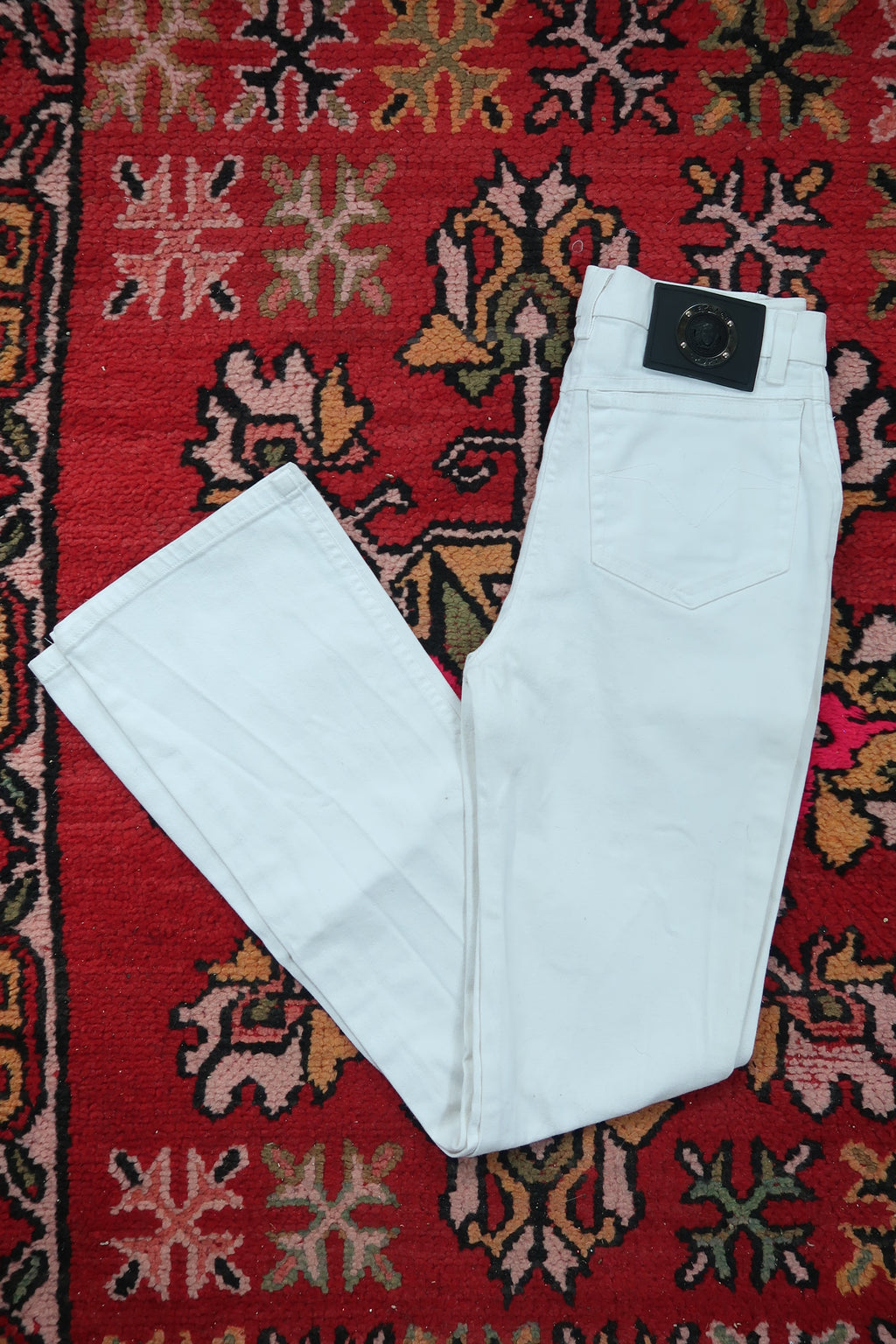 White vintage Versace Sport slim bootcut jeans for women, made in Italy, by Elektra Vintage, displayed on a hanger.