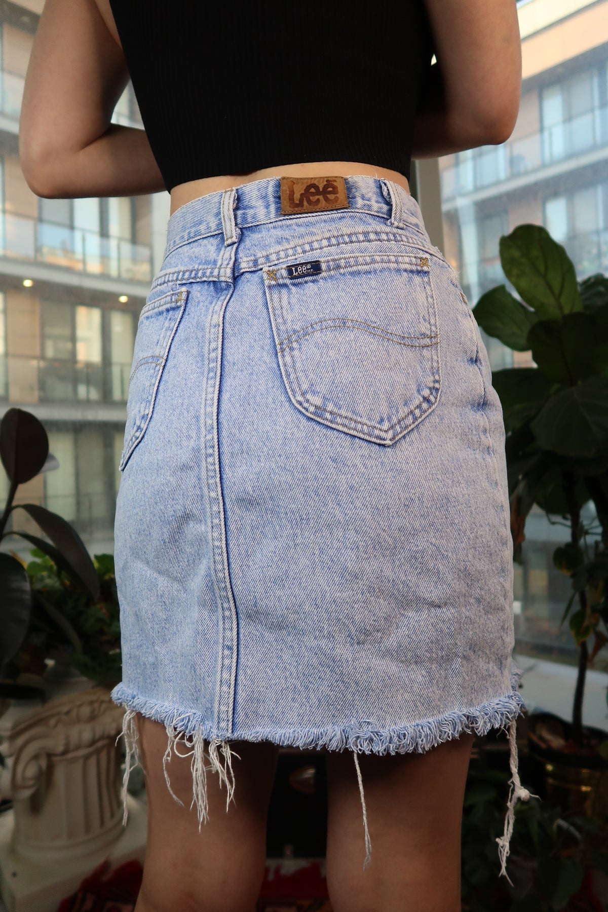 Light wash vintage 90s Lee denim mini skirt from Elektra Vintage, styled with a high waist and classic denim texture.