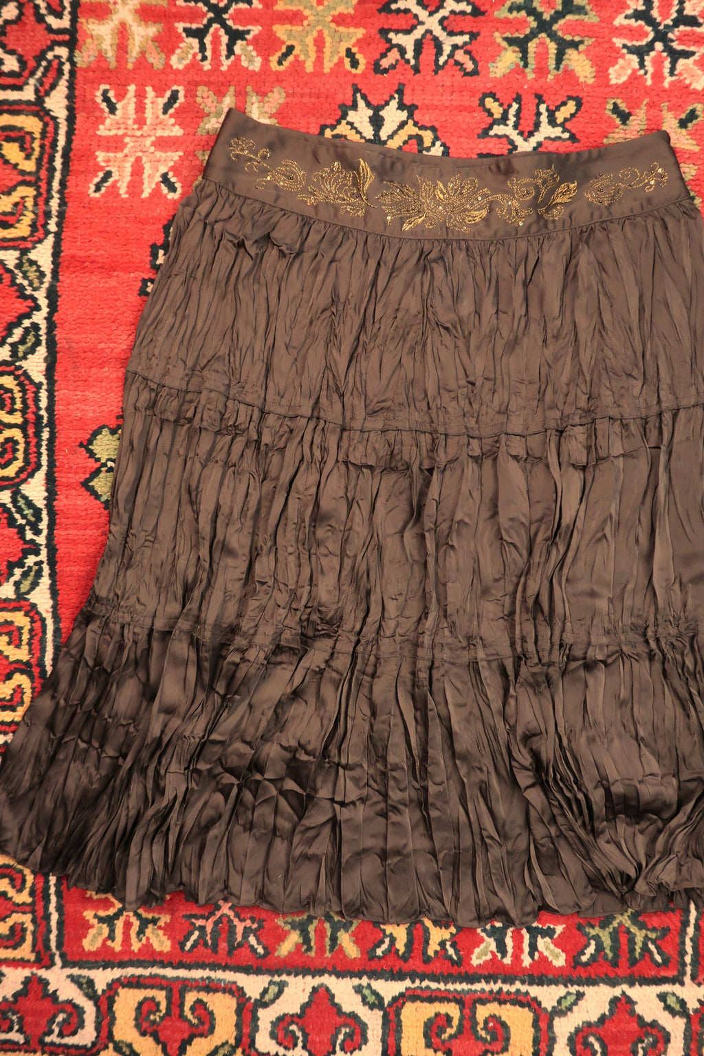 Vintage brown satin crepe midi skirt by Elektra Vintage with a gold embroidered waistband, shown hanging against a neutral background.