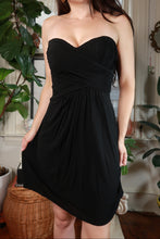 Load image into Gallery viewer, Black strapless pleated mini dress by BCBG, vintage 2000s style, with a sweetheart neckline and fitted waist, displayed on a hanger.
