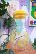 Vintage lemon print glass pitcher with yellow lid by Elektra Vintage, featuring retro citrus juice carafe design.