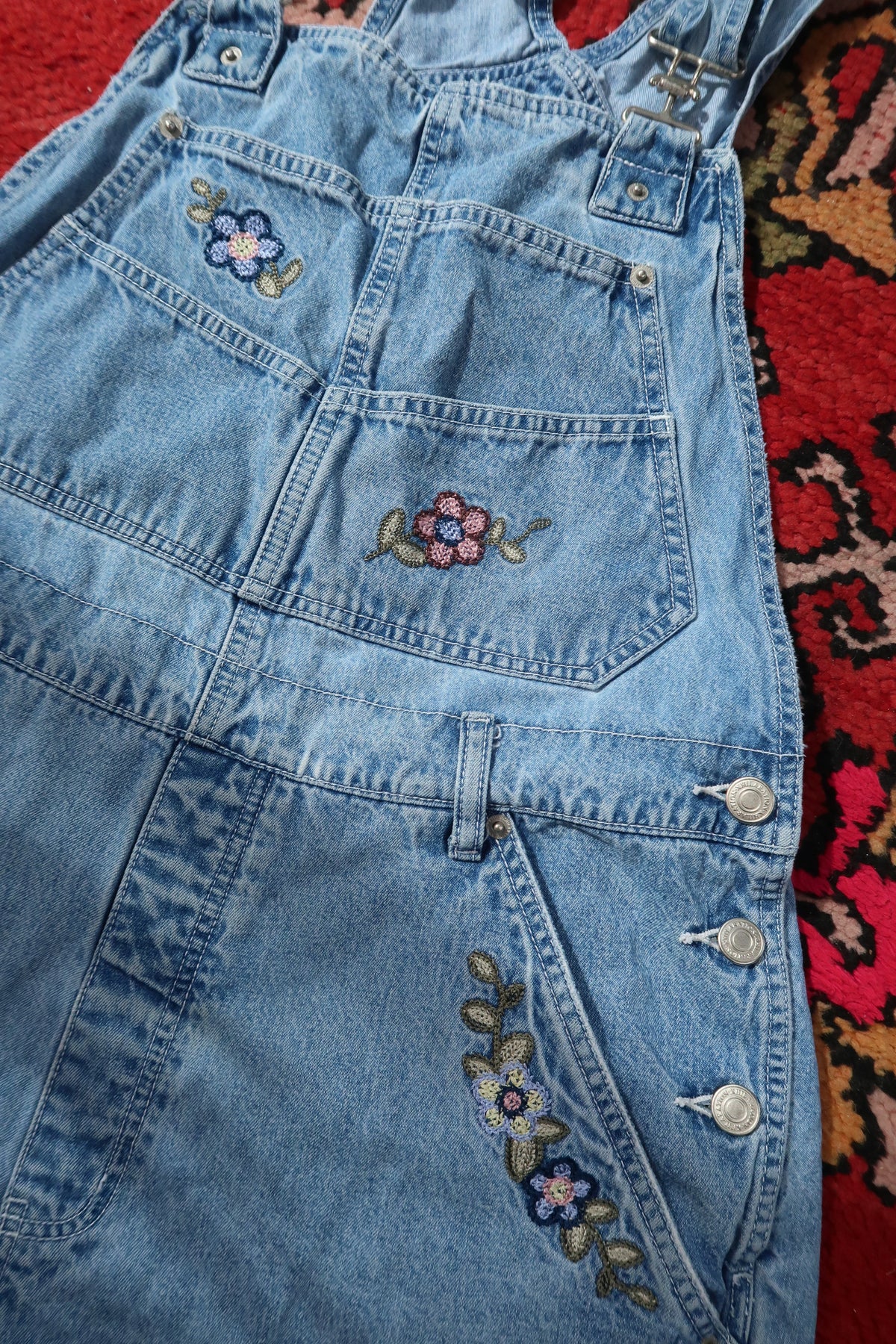 Vintage 1990s denim embroidered overall shorts dress with colorful floral embroidery, by Elektra Vintage, displayed on a hanger.