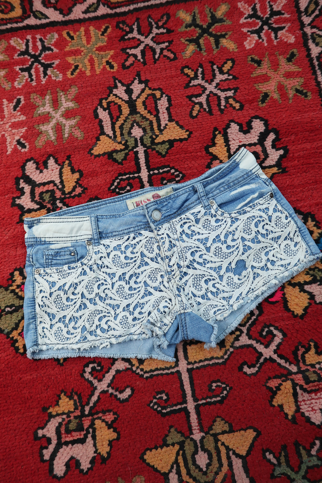 Women's vintage Y2K paisley lace denim shorts by Elektra Vintage, featuring distressed denim and intricate lace details.