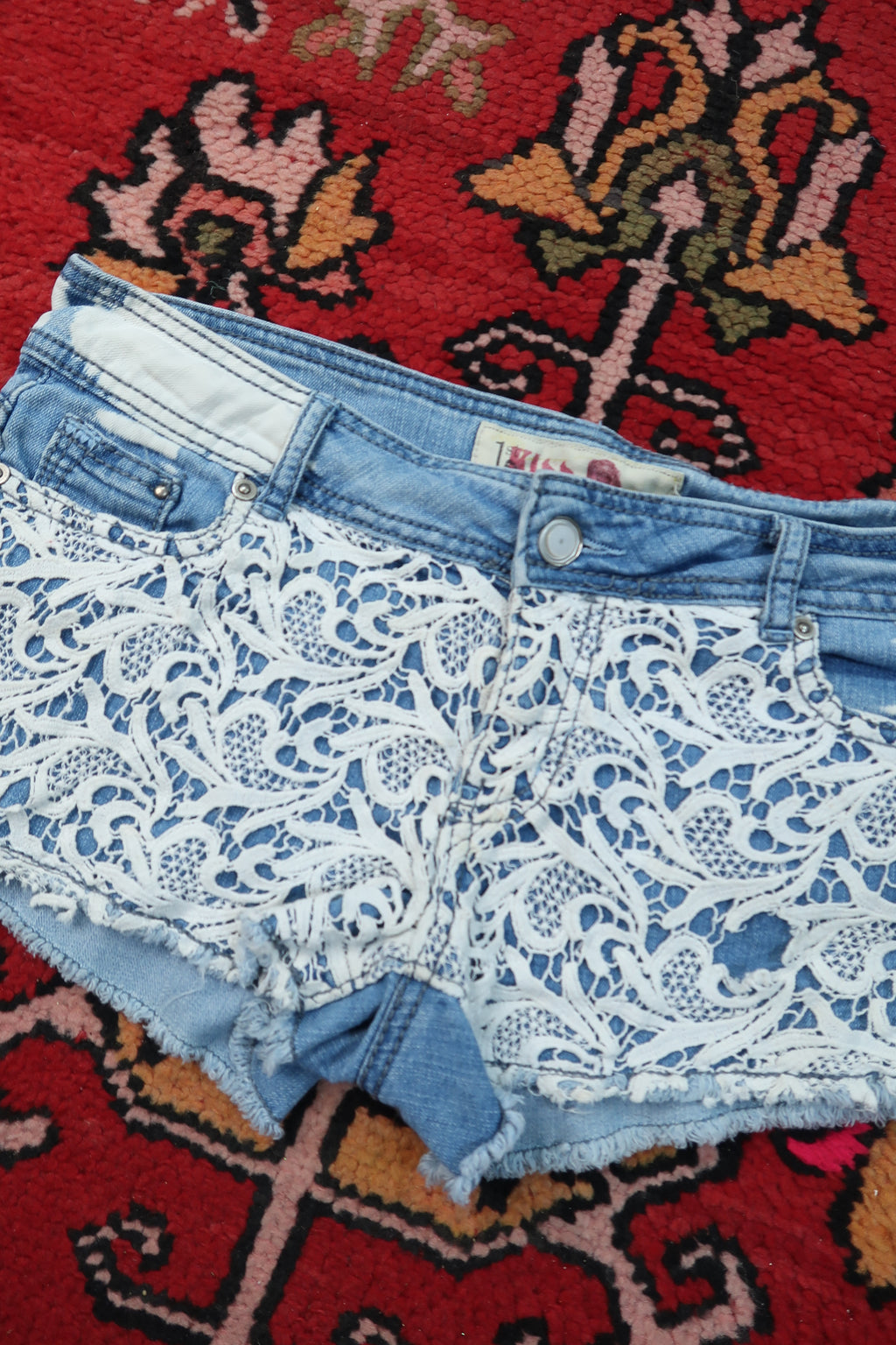 Women's vintage Y2K paisley lace denim shorts by Elektra Vintage, featuring distressed denim and intricate lace detailing.