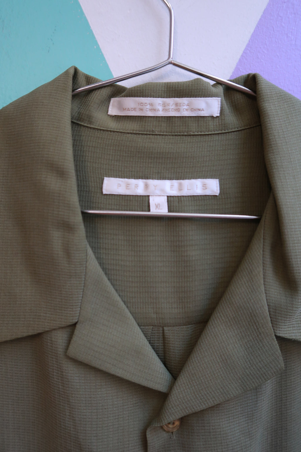 Vintage Perry Ellis silk olive camp shirt for men, displayed on a hanger with detailed fabric texture and classic collar.