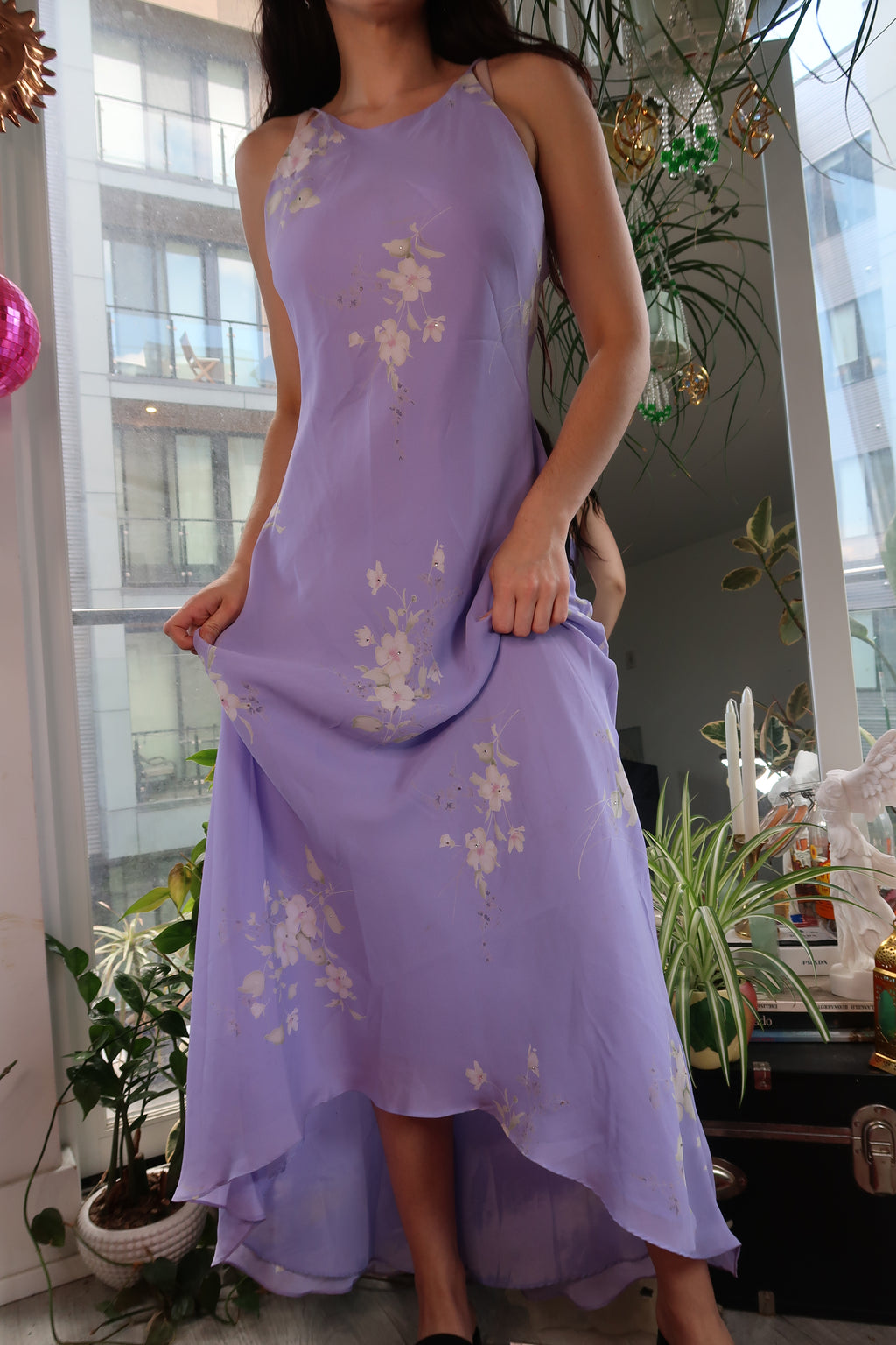 Person wearing a long, light purple dress with floral patterns indoors.